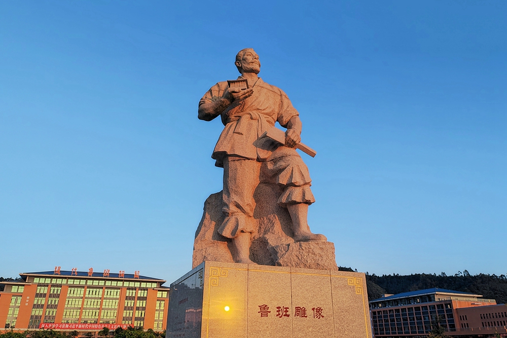 3,、魯班雕像（作者：宣傳統(tǒng)戰(zhàn)部）—巧圣稱寰宇，道器以化人,。魯班雕像,，向廣大師生傳揚著魯班的工匠精神和精湛工藝，讓魯班文化在廣東建院代代傳承,、發(fā)揚光大,。魯班雕像由惠州、佛山校友捐贈,，中國著名雕塑家林國耀創(chuàng)作,，采用福建惠安紅617石材制作，高6.957米,，重約50噸,。.jpg